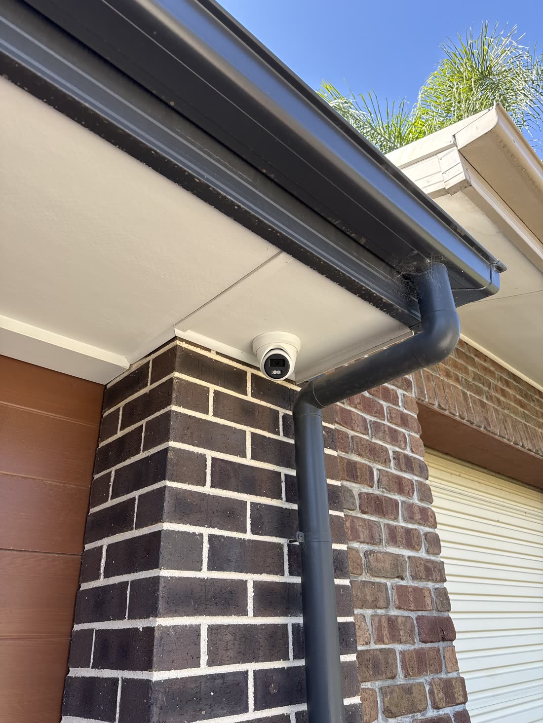 Turret security camera mounted under the eave on a brick pier, covering the driveway and garage approach, installed by Amped Up Electrical Adelaide