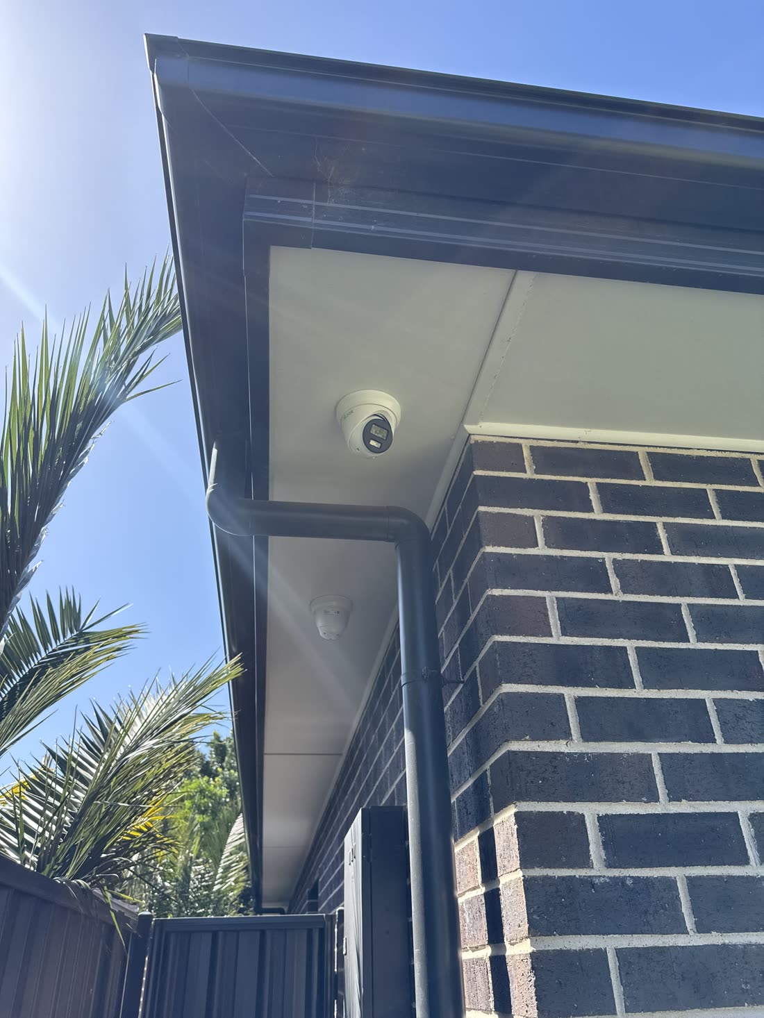 Security camera mounted under the eave covering a side gate approach, with a second camera further along the wall