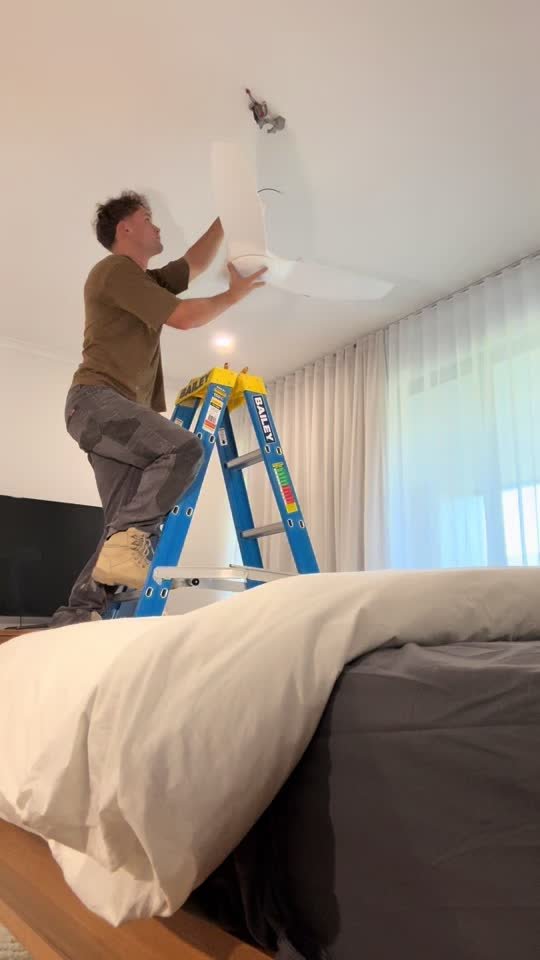 Marcus on ladder installing a flush-mount ceiling fan in an Adelaide bedroom